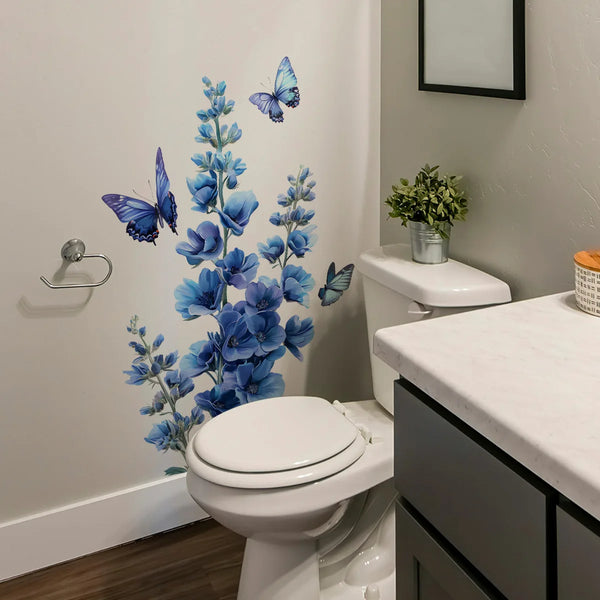 A white toilet features a blue flower and butterfly wall decal decoration on the surrounding wall.