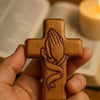 Handcrafted wooden prayer cross with detailed hand design, held in a person's hand.
