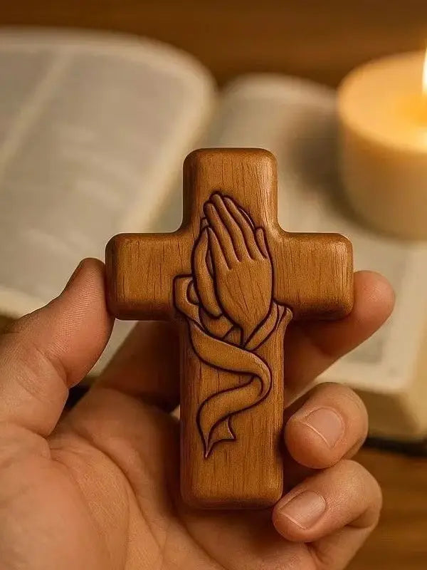 Handcrafted wooden prayer cross with detailed hand design, held in a person's hand.