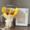 A bouquet of handmade crochet flowers featuring a teddy bear and various blooms, wrapped in yellow paper and tied with sheer 