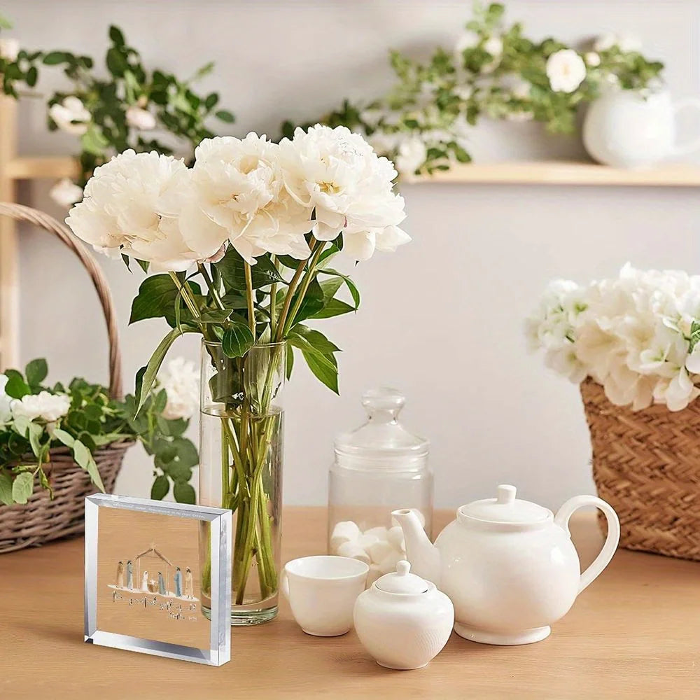 A clear glass vase holds white peonies next to a wooden shelf with ceramic teapot and small white decorative items.