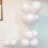 A cluster of white latex bow balloons with pink accents tied together on a white wall.