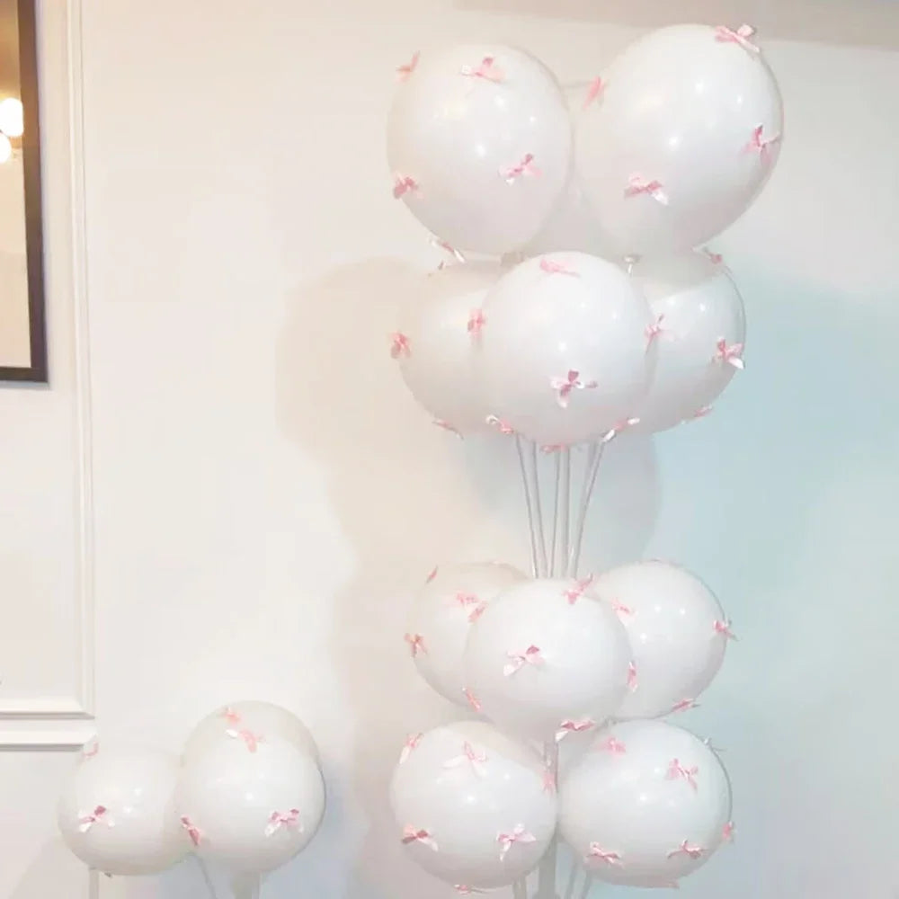 A cluster of white latex bow balloons with pink accents tied together on a white wall.