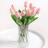 A bouquet of pink artificial tulips in a clear glass vase on a white plate.