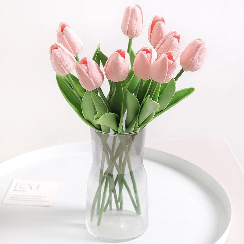 A bouquet of pink artificial tulips in a clear glass vase on a white plate.