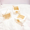 Three small kraft paper favor boxes tied with gold twine resting on white fabric.