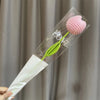 A clear plastic tube containing a pink crocheted tulip flower and a green stem, used for home decor or gifting.