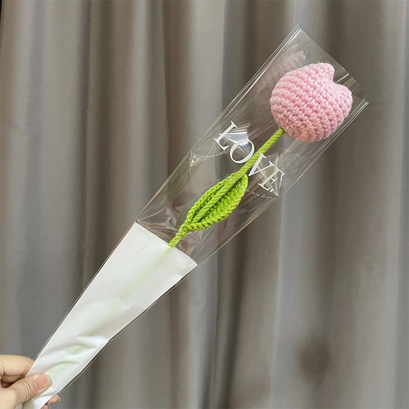 A clear plastic tube containing a pink crocheted tulip flower and a green stem, used for home decor or gifting.