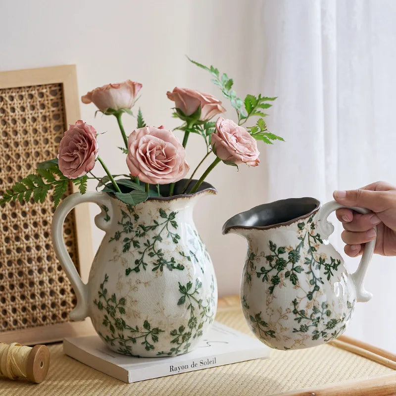 A rustic ceramic milk pitcher with a cracked glaze and pastoral design is held by a hand.