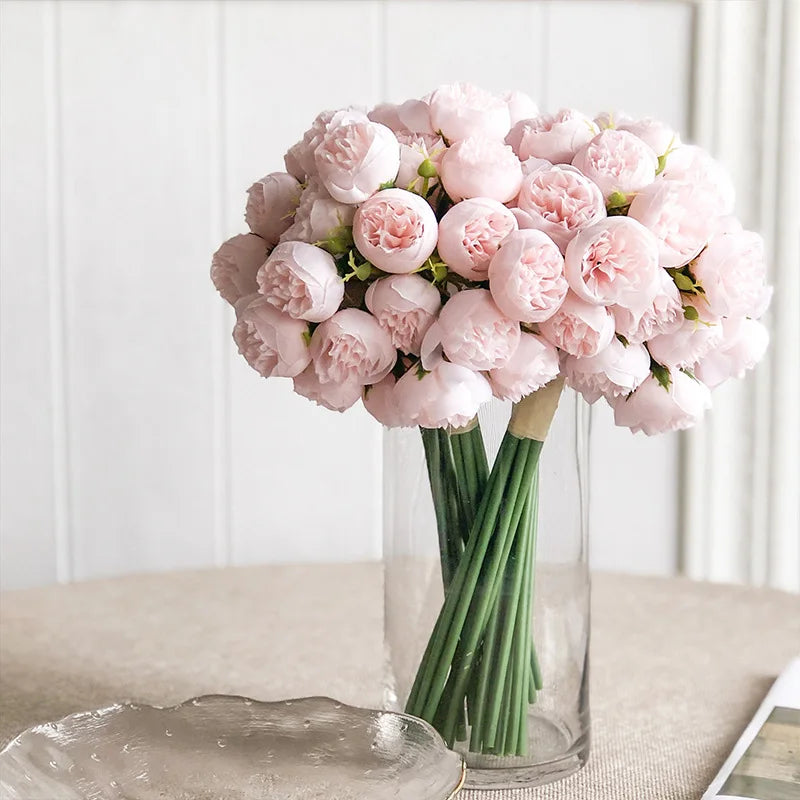 A bouquet of artificial pink peony silk flowers arranged in a clear glass vase.
