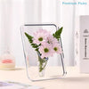 A clear acrylic frame holds a pink flower arrangement in a glass vase on a white surface.
