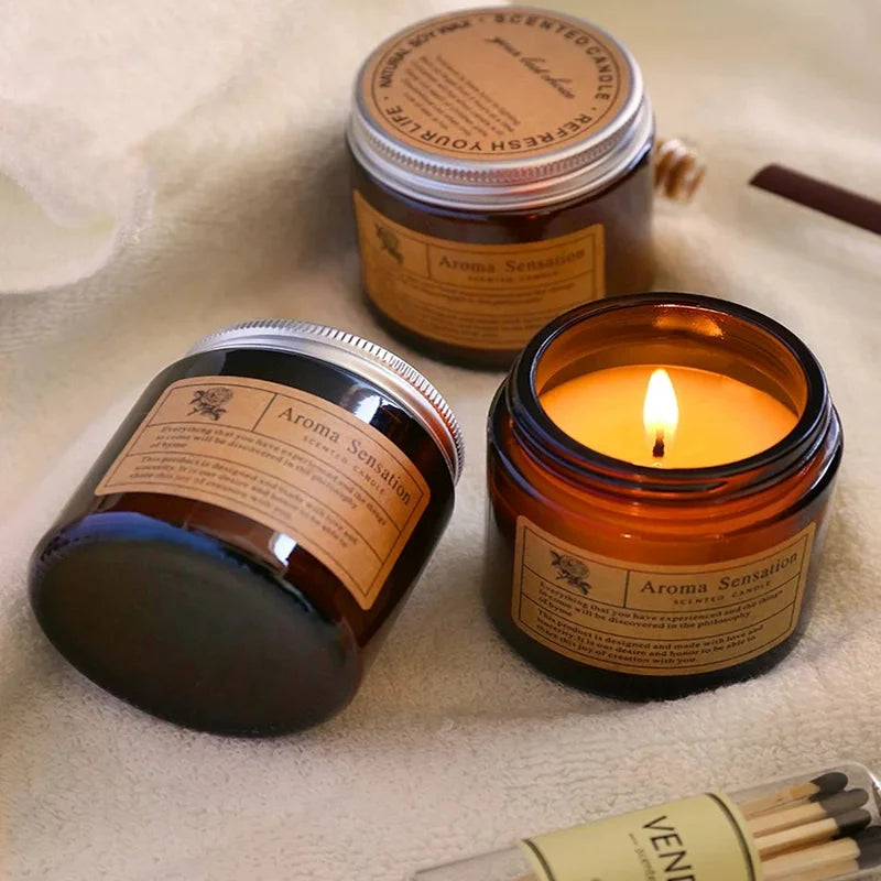 Two jars of Aroma Sensation scented candles are displayed on a white towel with a wooden matchstick.