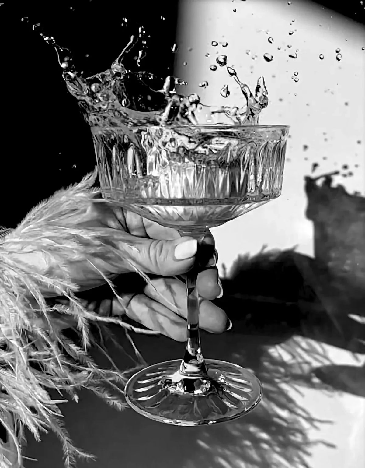 A hand holds a glass of liquid, causing splashes, in a black and white photograph.