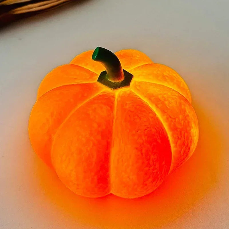 An orange decorative LED pumpkin night light with a green stem resting on a white surface.