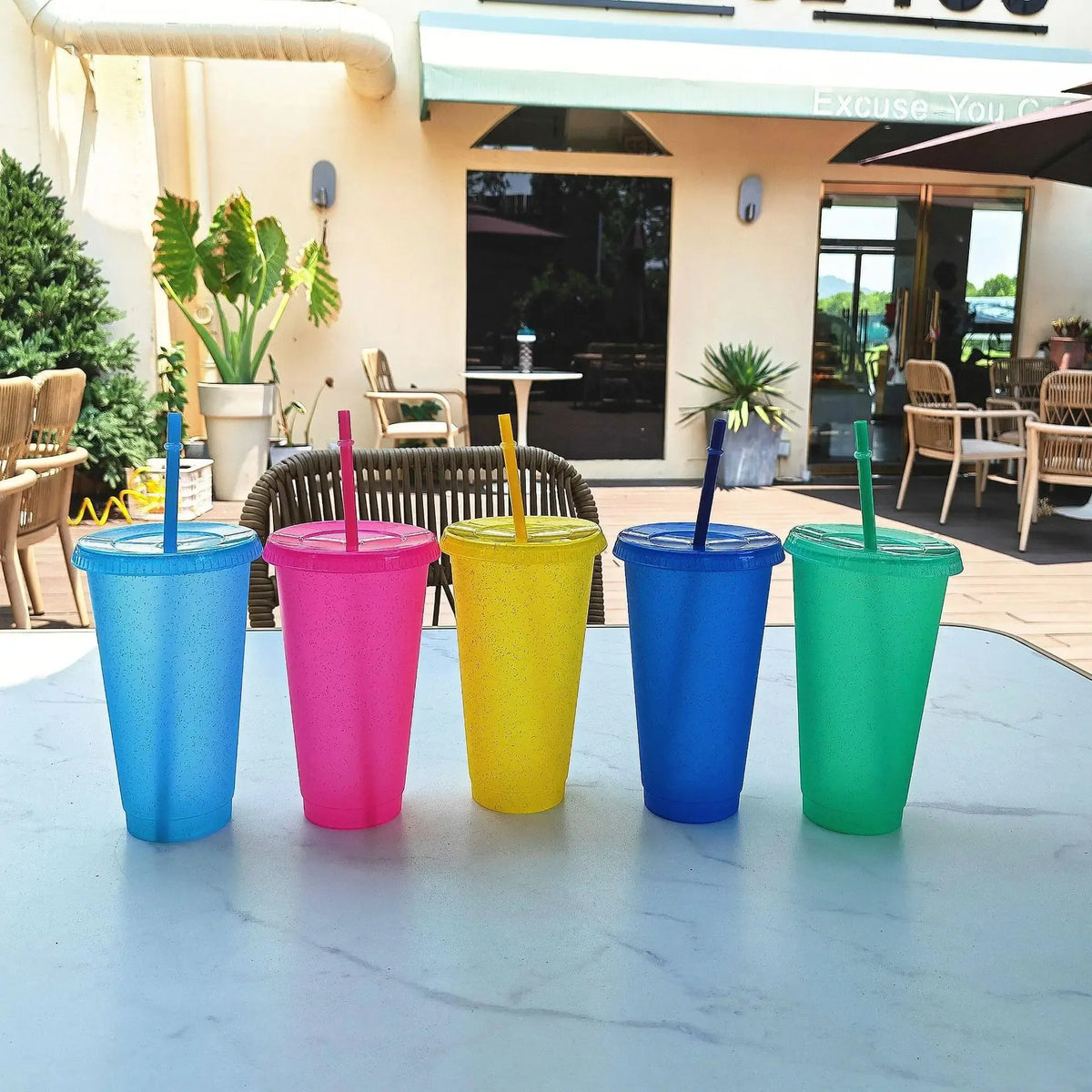 Five colorful plastic cups with lids and straws arranged on a light blue table.
