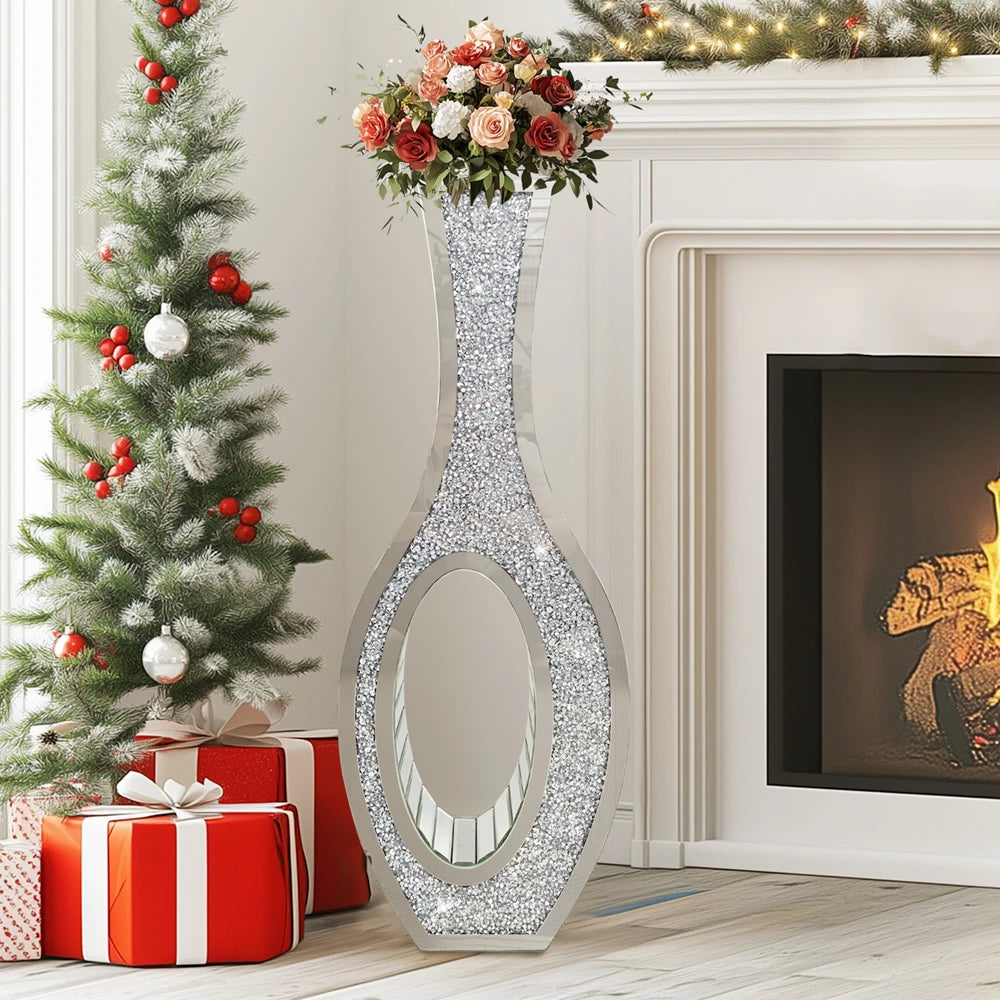 Tall silver mirrored vase with crushed diamond finish displayed in a white fireplace setting next to a decorated Christmas tr