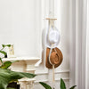 A bohemian macrame hat hanger made of natural fibers is displayed on a white wall, hanging next to a wooden rod.