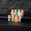 A collection of small glass bottles filled with colorful glitter powder for party decorations arranged on a dark surface.