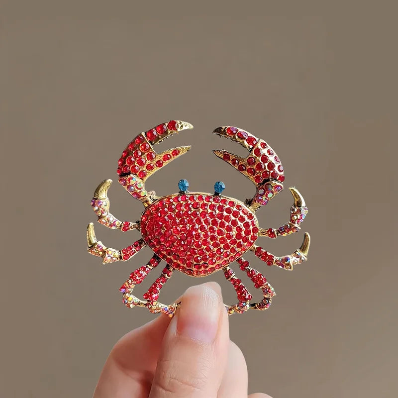 A close-up of a vintage marine life brooch pin set featuring a vibrant red crab design being held by a hand.