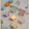 A collection of handmade soy wax flower tea light candles in various pastel colors arranged on a white surface.