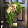 A rustic green hydrangea wreath with a burlap bow hangs on a dark door.