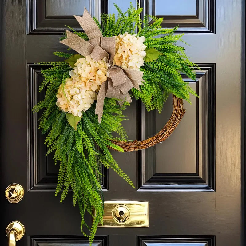 A rustic green hydrangea wreath with a burlap bow hangs on a dark door.