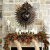 A dark bronze sacred heart wall plaque surrounded by rays mounted on a stone wall above a floral wreath