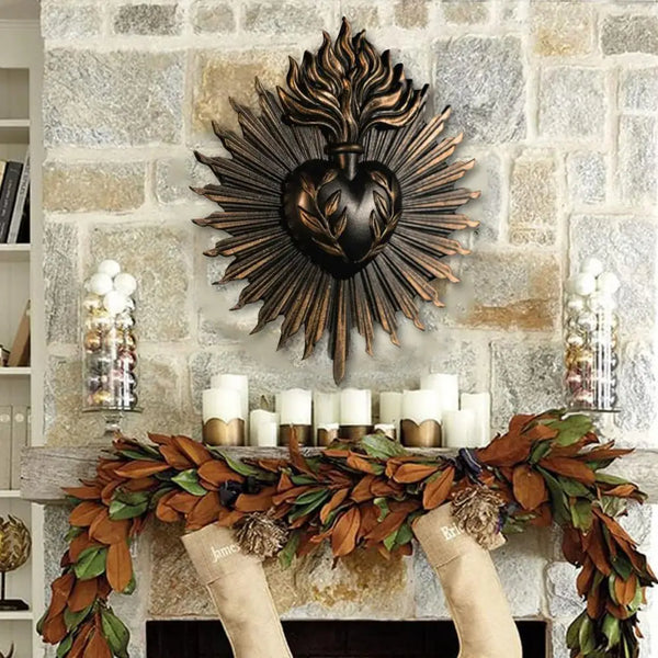 A dark bronze sacred heart wall plaque surrounded by rays mounted on a stone wall above a floral wreath