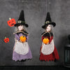 A pair of witch ornaments featuring a black pointed hat, gray hair, and harvest-themed clothing in purple and red.