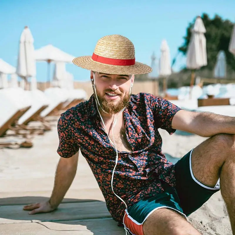 A man wearing a straw hat and a patterned shirt sits outdoors on a wooden surface.