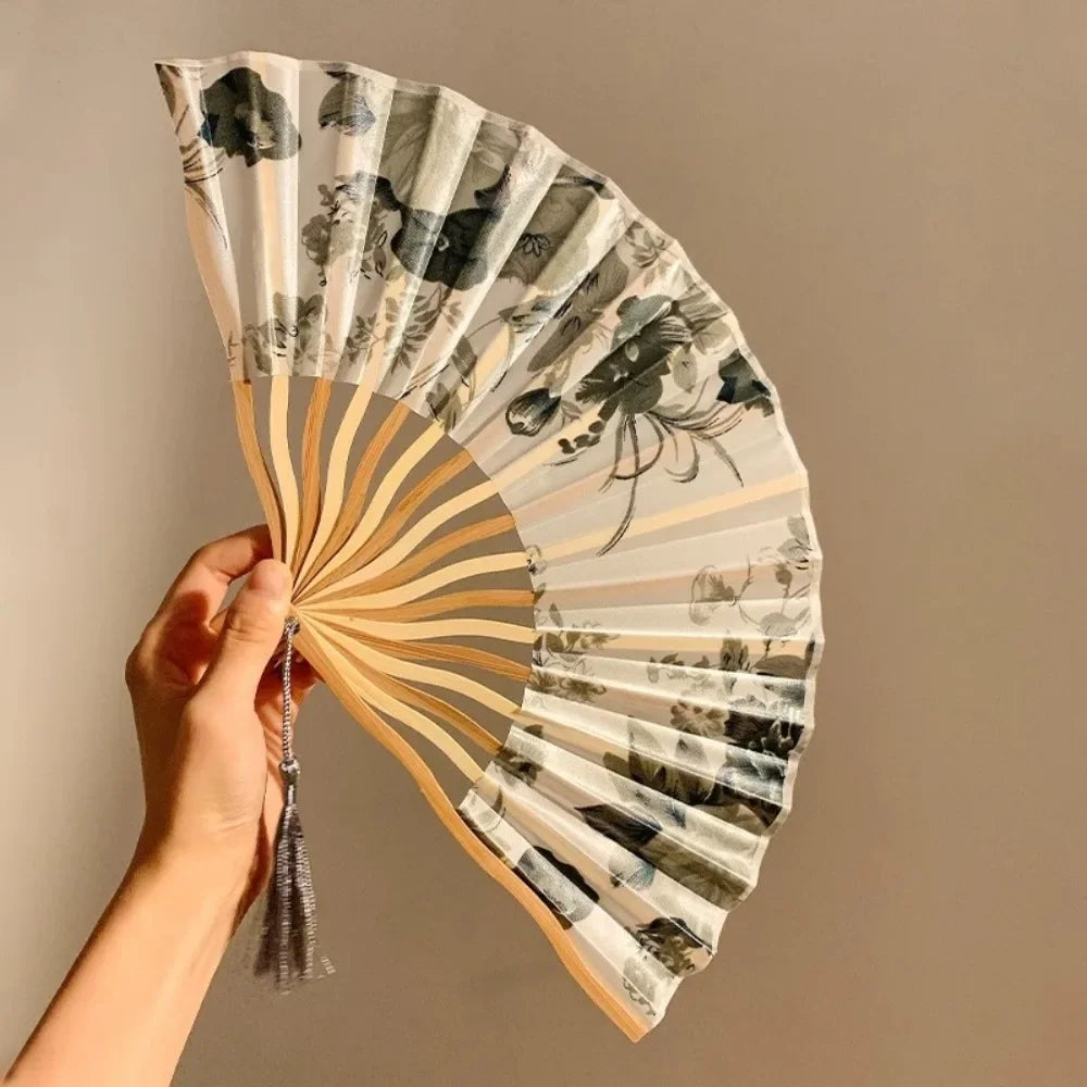 A hand is holding an open folding fan with a leopard print design and black handle.