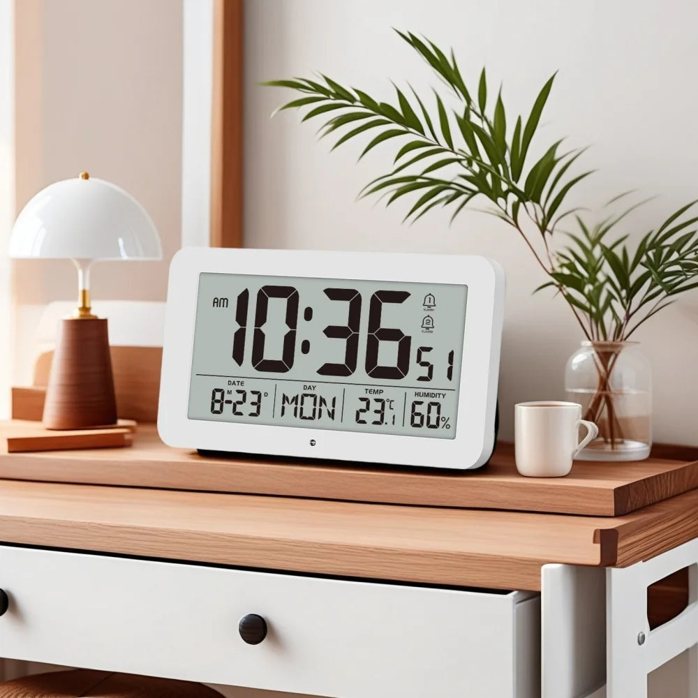 A white digital wall clock displaying 10:36 AM, temperature, and humidity, sitting on a wooden surface next to a potted plant