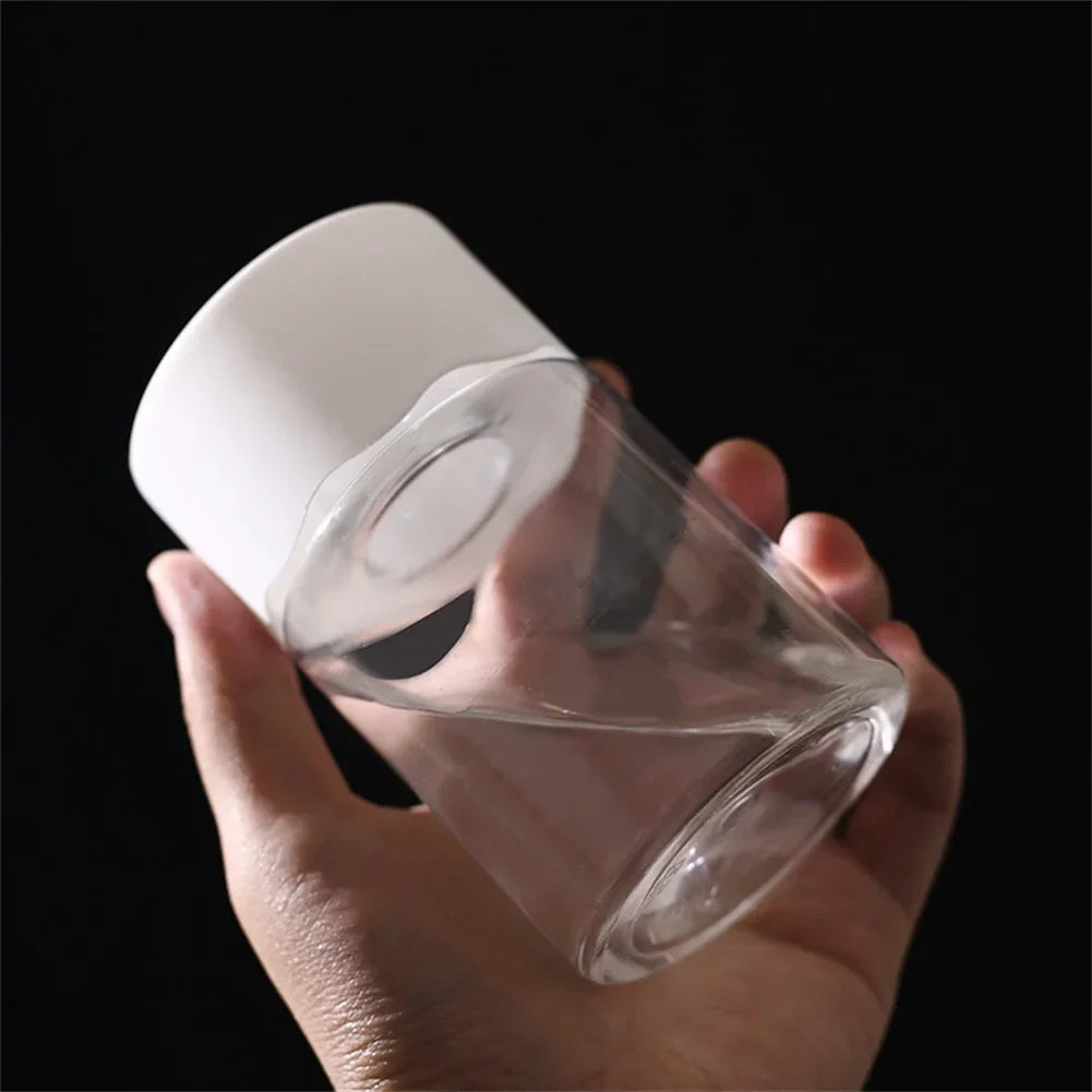 A hand holds a clear mini hydroponic glass planter for indoor plants against a dark background.