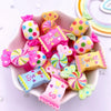A pink dish filled with colorful candy resin cabochons in various shapes and colors for crafting projects.