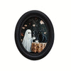 Oval framed wall art depicting a ghost figure and a black cat drinking tea on a draped table.