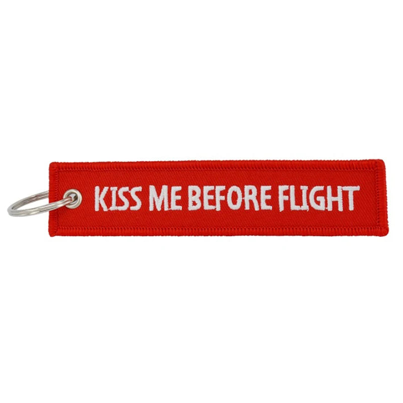 Red woven keychain with white text that reads Kiss Me Before Flight