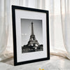 A framed black and white photograph of the Eiffel Tower displayed against a white curtain backdrop.