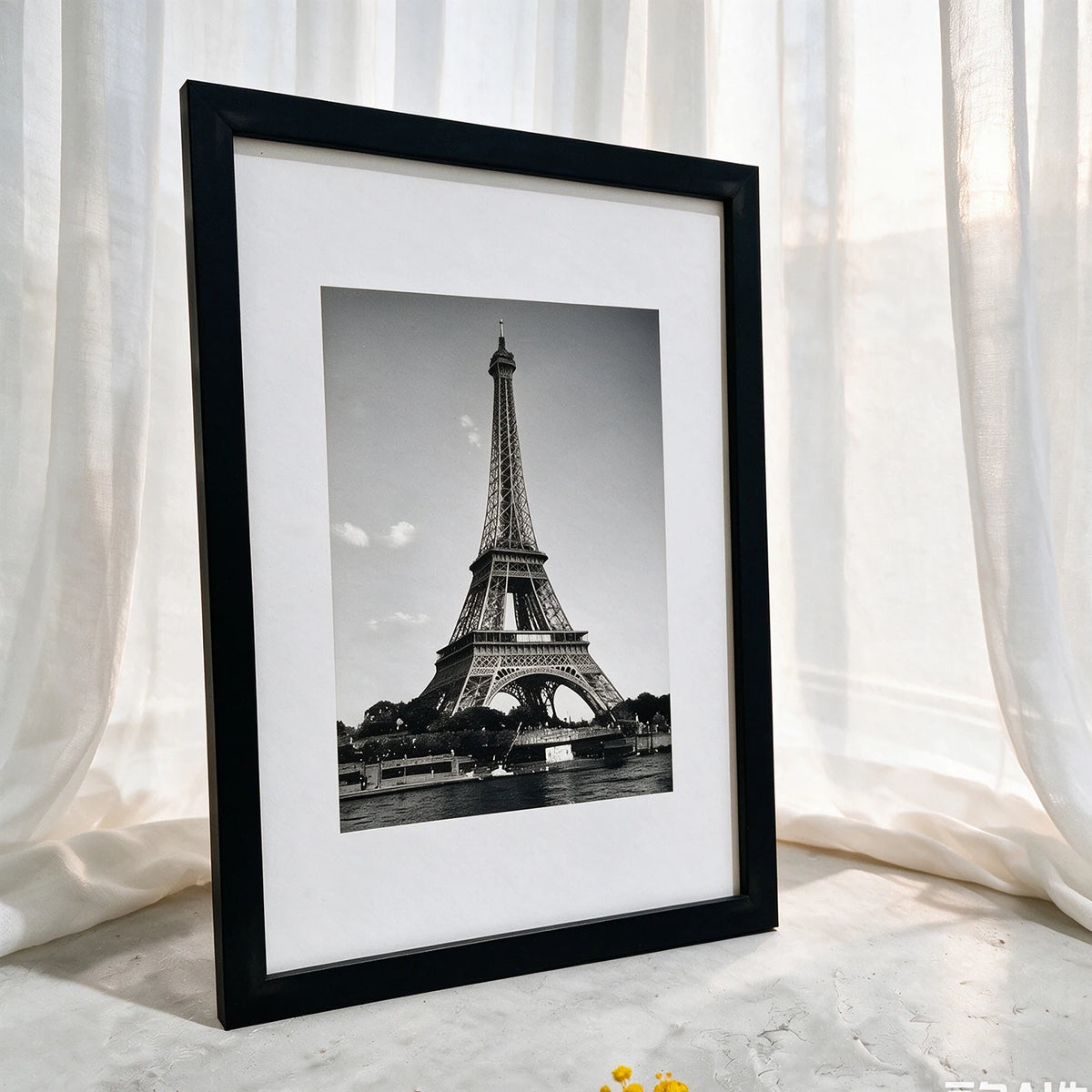 A framed black and white photograph of the Eiffel Tower displayed against a white curtain backdrop.