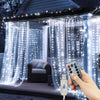 A hand holds a remote control for LED curtain fairy lights illuminating sheer curtains on a window.