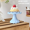 A mini blue cupcake stand displaying a single cupcake topped with red berries and cream on a wooden surface.