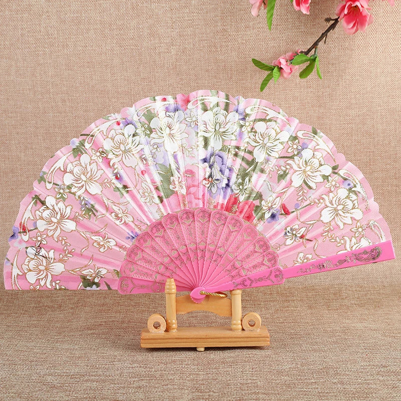 Pink silk flower folding fan with white and purple floral patterns displayed on a wooden stand.