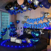 A dark room decorated with blue and silver balloons forming a happy birthday banner above a bed.