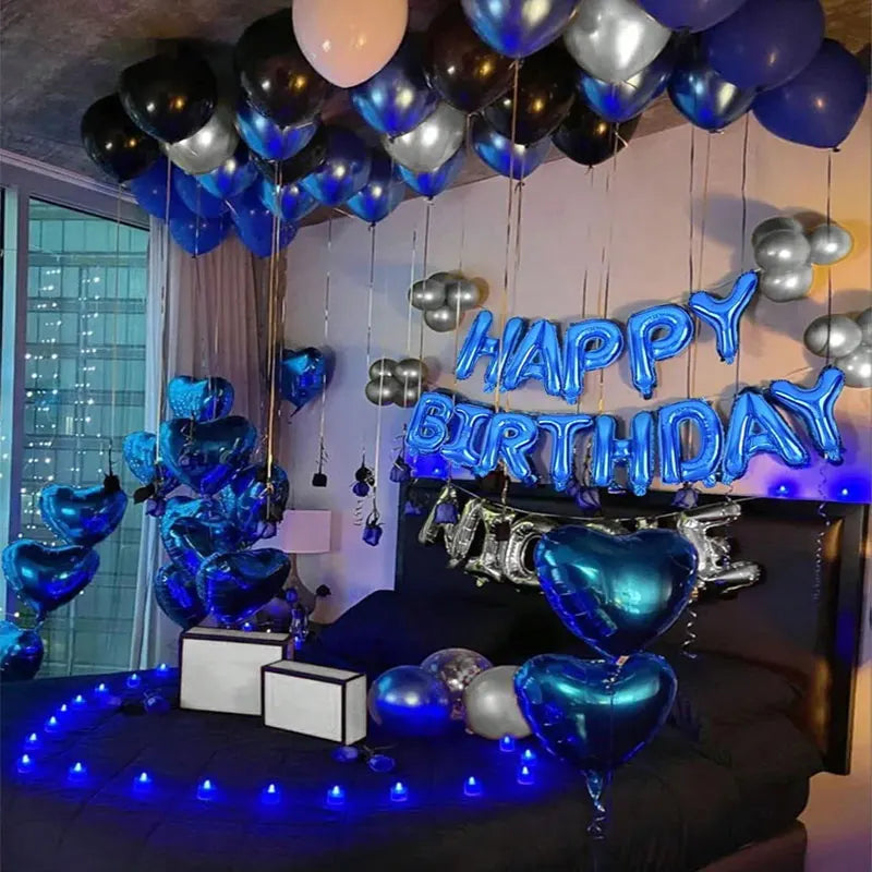 A dark room decorated with blue and silver balloons forming a happy birthday banner above a bed.