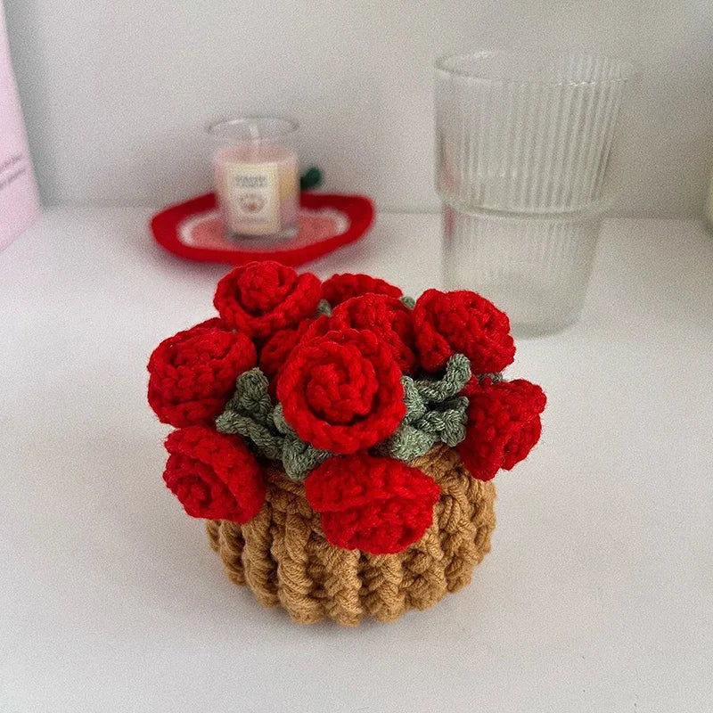 A cluster of hand-crocheted red rose flowers with green leaves in a woven natural fiber pot.