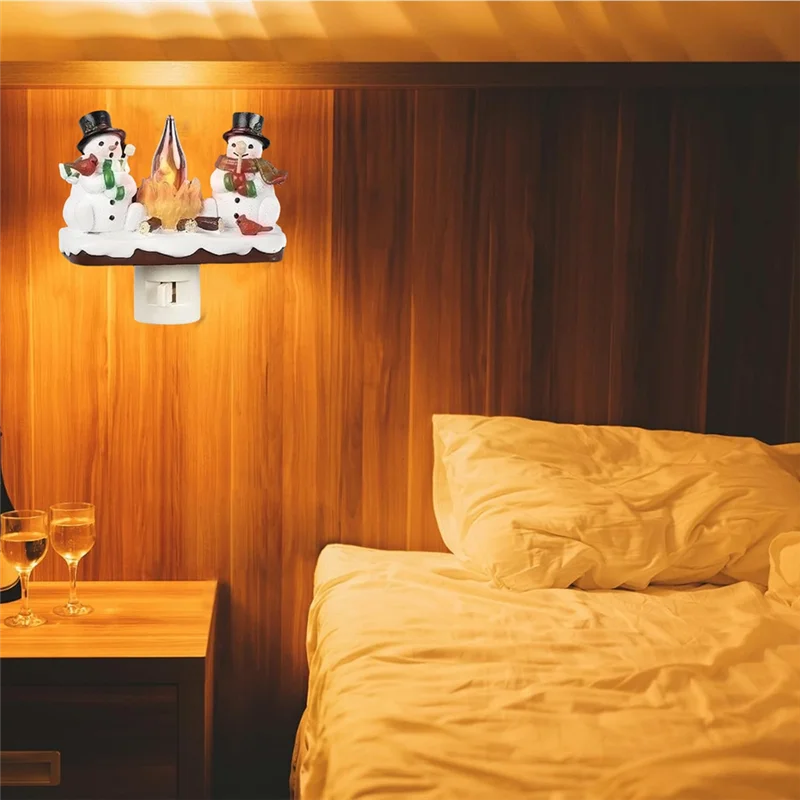 A night light decoration featuring snowmen and a flickering campfire on a wooden panel.