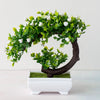 An artificial bonsai tree decoration with bright green leaves and white blossoms growing from a dark brown trunk in a white p