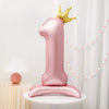 A large pink foil balloon shaped like the number one stands on a white pedestal with a gold crown above it.