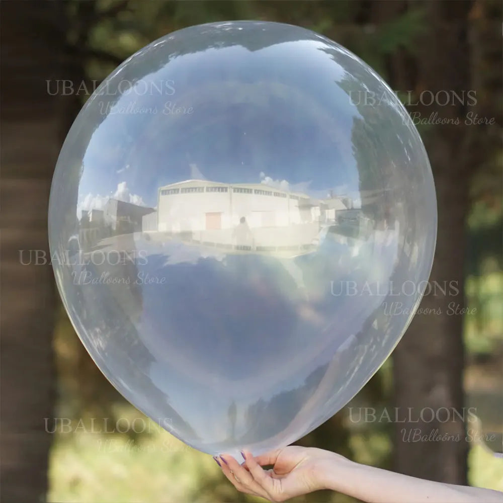 A hand holds a large, clear latex balloon reflecting an outdoor landscape.