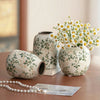 A handmade ice crackle ceramic vase with white and green floral patterns sits on a wooden surface.