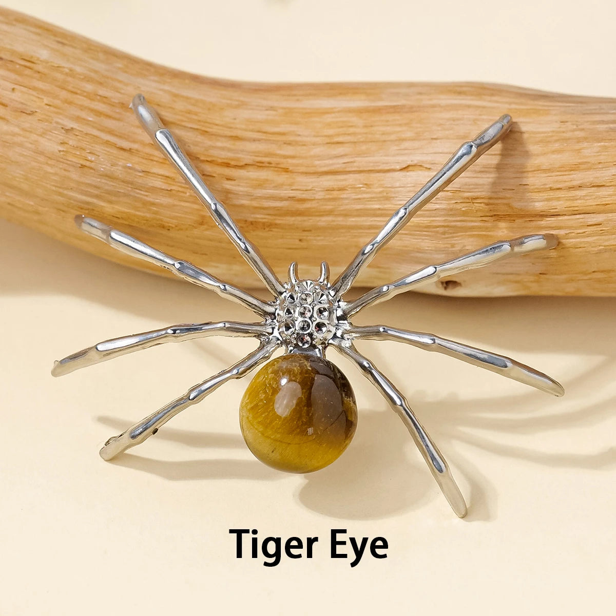 Silver crystal spider figurine with a golden tiger eye bead resting on a natural wood surface.